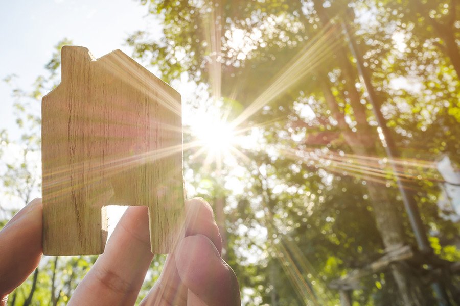 Cut out of a home made of timber with the sun and trees in the background.