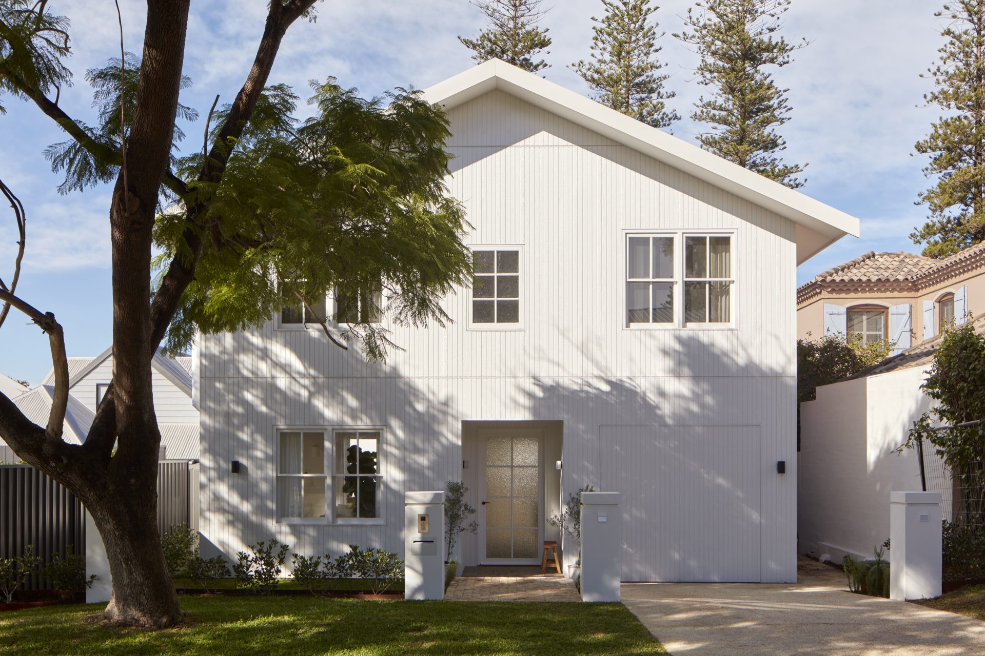 Front of newly built White stained wood cladded panels home. Big tree in front yard.